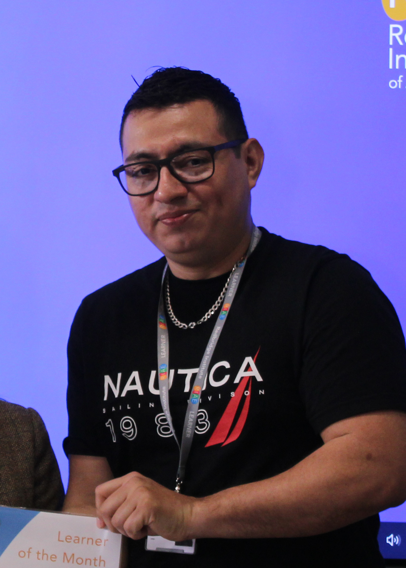 A photo of Luis Gilberto Rivas Munoz holding a learner of the month certificate wearing a Redbridge lanyard.