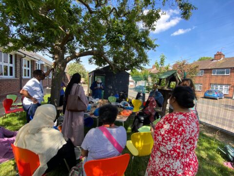 People outside, under a tree, gathered around a table with various gardening items and tools.