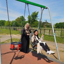 A woman sitting at a swing in the park and another woman pushing her