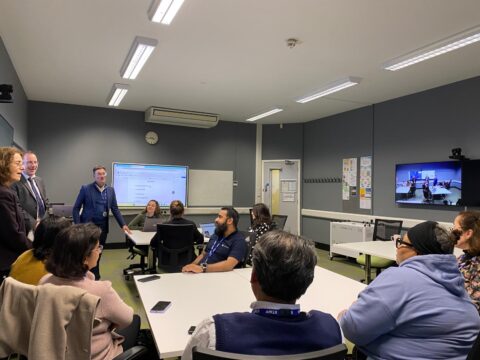 People sitting in a classroom listening to 3 people give a talk