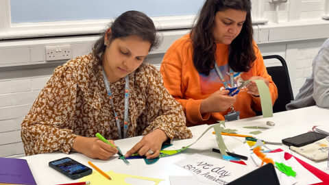 Two women sitting at a table, colouring on paper