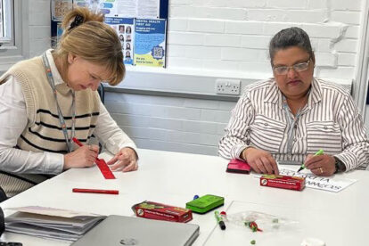 Two women, sitting at a table, colouring with markers