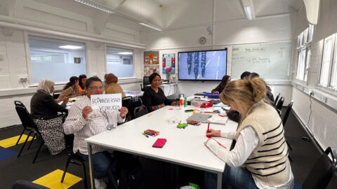 People in a classroom, sitting around a table and crafting with paper