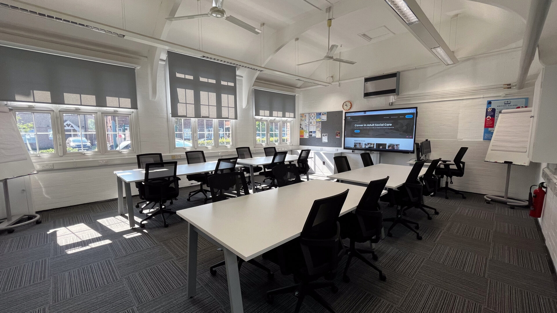 A room with white tables. black officer chairs and a large screen in the back