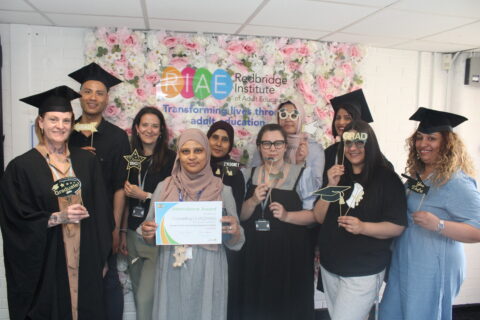 People in front of a wall of flowers wearing graduation caps and gowns
