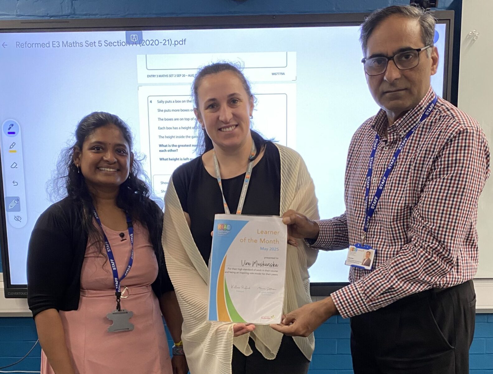 Three people posing for the camera. The woman in the middle is being presented with a certificate
