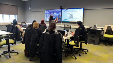 People sitting at tables, looking at two large screens