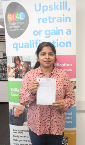 Learner standing in front of Redbridge Institute banner holding a paper with her GCSE exam results