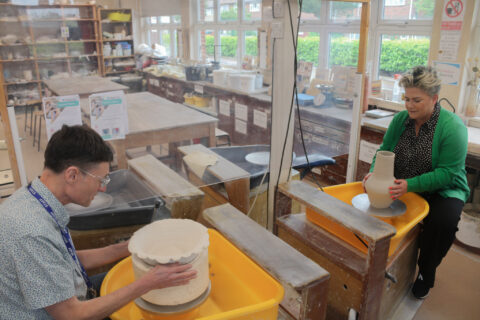 Man and woman using separate pottery wheels to make vases