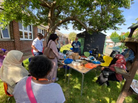 People outside, under a tree, gathered around a table with various gardening items and tools.